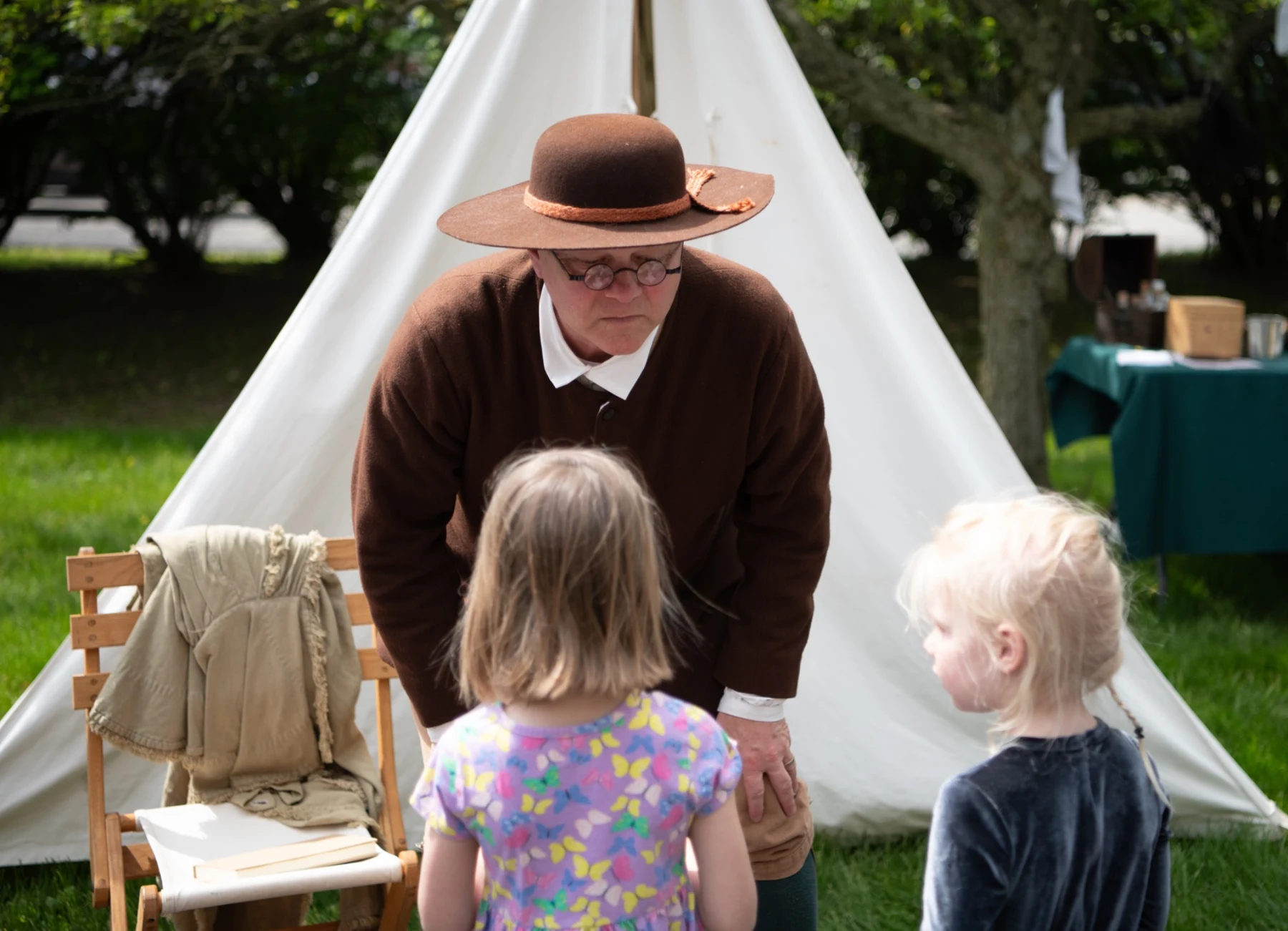 An interpreter speaks with two young visitors beside a canvas tent.
