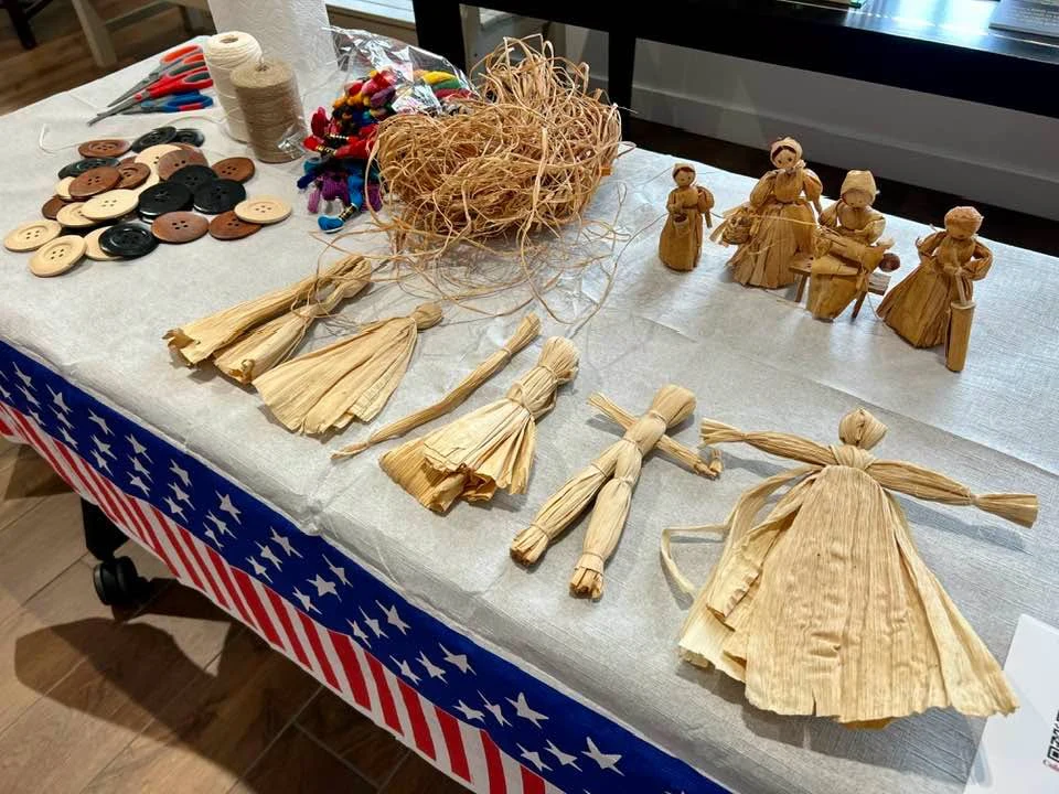 Corn husk dolls and craft materials displayed on a table.